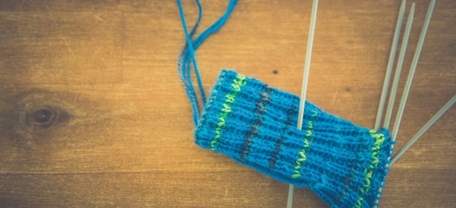 A set of double-pointed needles holds a green and blue knitting project, likely a sock.